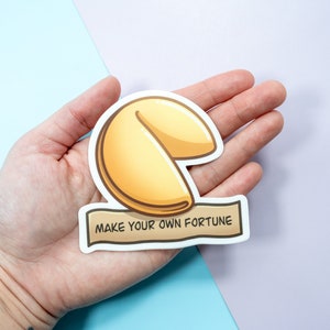May include: A white sticker with a cartoon illustration of a fortune cookie and the text "Make your own fortune".