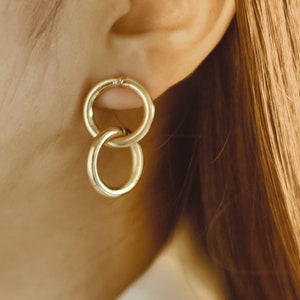 May include: Gold double hoop earrings with a simple design. The earrings are made of two interlocking hoops.
