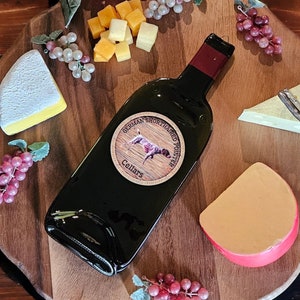 May include: A wooden serving board with a bottle of wine, grapes, and various cheeses. The bottle has a label that says "Fox Run Cellars Cabernet Sauvignon".