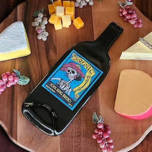 May include: A wooden cheese board with a bottle of wine, grapes, and various cheeses. The bottle is a dark blue glass bottle with a label that says "Joya King Reino".