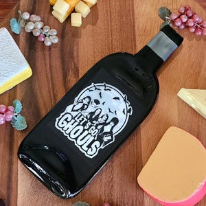 May include: Black wine bottle shaped serving tray with a white graphic of a full moon and four figures with the text "Let's go Ghouls".