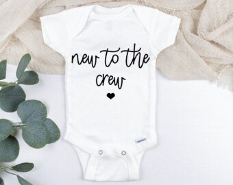 May include: White baby onesie with black text that reads "new to the crew" and a small black heart.