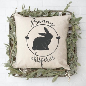 May include: A white pillow with the text "Bunny whisperer" and a black silhouette of a bunny rabbit inside a circle with two hearts.