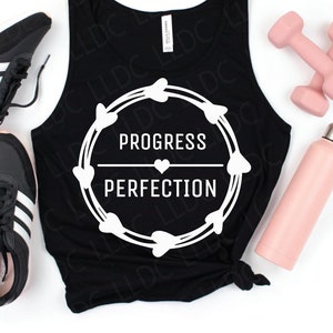 May include: Black tank top with a white graphic that says "Progress over Perfection" in a circle with hearts around it. The tank top is laying on a white surface with a pair of black sneakers, a pink water bottle, and pink dumbbells.