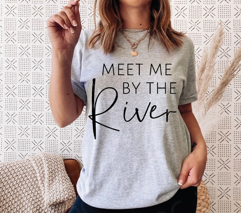 Op de afbeelding: Grijs T-shirt met zwarte tekst die "Meet me by the river" zegt.