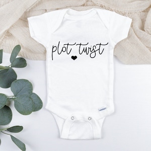 May include: White baby onesie with black text that reads "plot twist" and a small black heart.