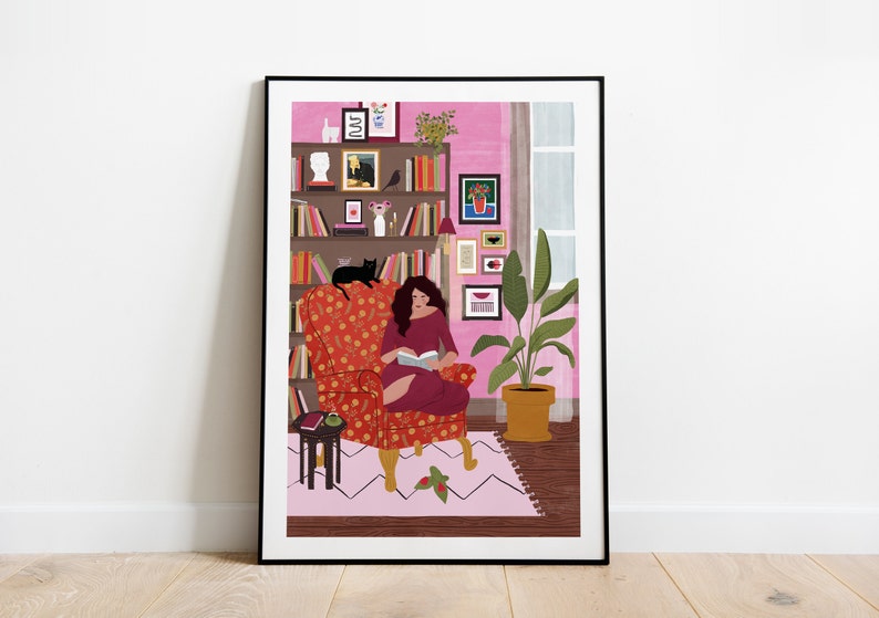Puede incluir: Una mujer se sienta en un sill&oacute;n rojo con estampado floral, leyendo un libro. Un gato negro se sienta en el respaldo del sill&oacute;n. La habitaci&oacute;n tiene una pared rosa, una estanter&iacute;a con libros y objetos decorativos, y una planta en maceta.