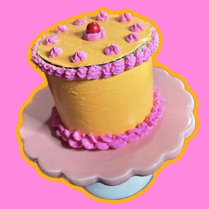 May include: A yellow cake with pink frosting and a red cherry on top. The cake is on a pink cake stand.