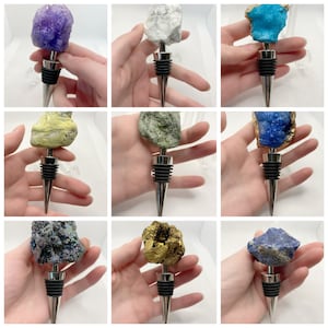 Pode incluir: Nove rolhas de garrafa diferentes com várias tampas de pedra natural. Cada rolha tem uma base de metal prateado e uma ponta pontiaguda. As pedras incluem ametista, ágata branca, turquesa, lápis-lazúli, aventurina verde, jaspe amarelo, druzy dourado e druzy azul.