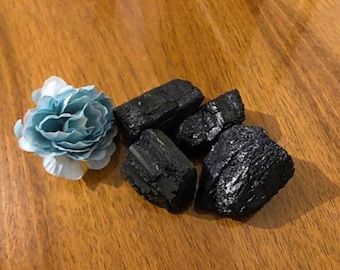 Peut inclure: Cinq cristaux de tourmaline noire sur une surface en bois. Les cristaux sont bruts et ont un aspect naturel non poli.