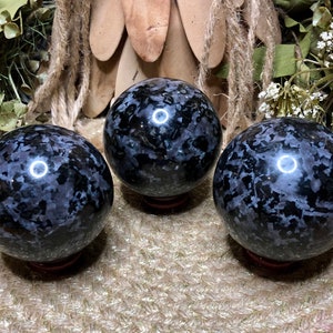 May include: Three polished black and white snowflake obsidian spheres on wooden stands. The spheres are approximately 2 inches in diameter.