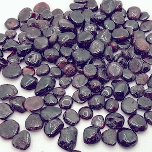 May include: A large collection of dark red, polished, gemstone chips. The chips are various sizes and shapes, and have a smooth, glossy finish.