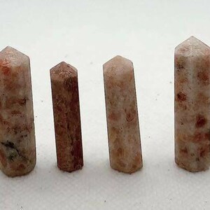 Pode incluir: Uma coleção de oito pontas de cristal de pedra do sol em vários tamanhos, que vão do rosa claro ao laranja com um efeito brilhante e iridescente.