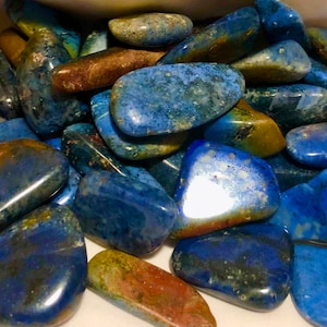 May include: A collection of tumbled blue lapis lazuli stones. The stones are smooth and polished, with a variety of shades of blue and green. They are perfect for use in jewellery making, crystal healing, or as decorative accents.