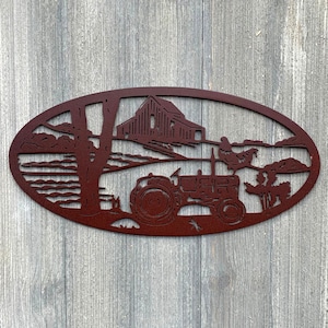 May include: A rusty red metal oval wall decoration featuring a silhouette of a farmhouse, a tractor, and trees. The farmhouse has a barn door and a window. The tractor has a large wheel and a smaller wheel. The trees are stylised and have branches.