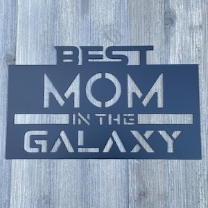 May include: Black metal sign with the text "BEST MOM IN THE GALAXY" in a stylized font.