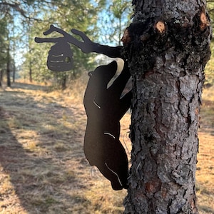 May include: A black metal silhouette of a bear climbing a tree with a honeycomb hanging from a branch. The bear is reaching up towards the honeycomb.