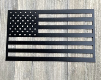 May include: A black metal American flag wall decoration with a cut-out design. The flag has 13 horizontal stripes and 50 stars.
