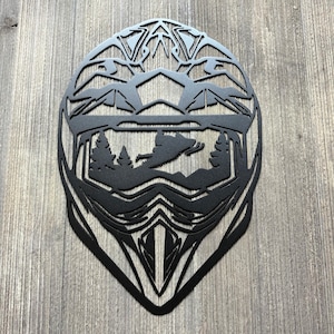 May include: Black metal silhouette of a snowmobile helmet with a snowmobile rider and trees visible through the visor.