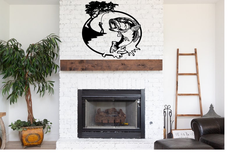 Puede incluir: Arte de pared de metal negro que representa un pez perca saltando fuera del agua con un pescador en el fondo. El arte est&aacute; montado sobre una chimenea.