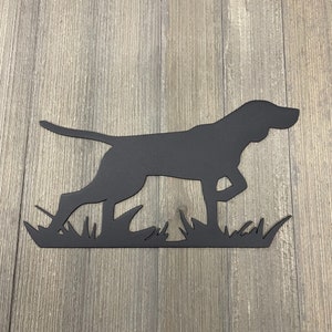 May include: Black metal silhouette of a German Shorthaired Pointer dog running through tall grass. The dog is facing right and has its tail raised. The silhouette is cut out of metal and mounted on a wooden background.
