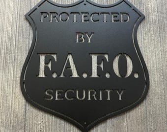 Puede incluir: Señal de metal negro con forma de escudo con el texto "PROTECTED BY F.A.F.O. SECURITY" en blanco.