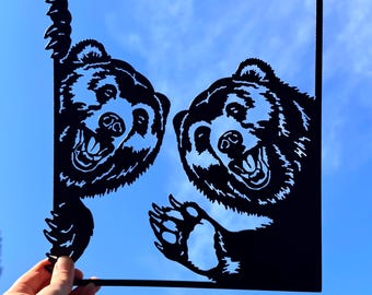May include: Black metal artwork depicting two smiling bear faces within a rectangular frame. One bear peeps from the left, the other from the right, against a blue sky. The bears have open mouths and detailed fur.