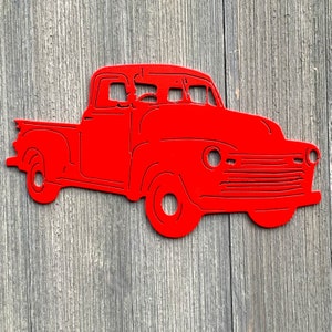 May include: Red metal cutout of a vintage pickup truck. The truck has a flatbed and a rounded cab. The truck is a popular design element for home decor.