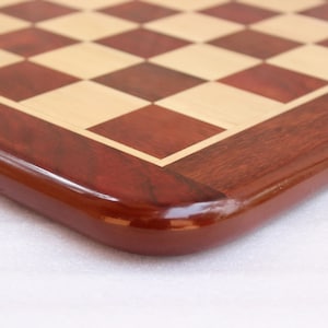 May include: Close-up of the corner of a wooden chessboard with a red mahogany finish. The board has a light wood inlay for the squares.