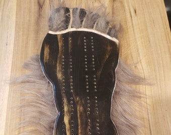 May include: A wooden game board shaped like a footprint with a brown fur trim. The board has a black background with rows of holes for pegs.