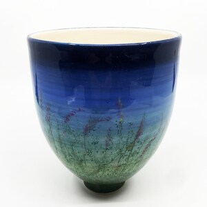 May include: A blue and green ceramic vase with a gradient design and a floral pattern. The vase has a wide mouth and a narrow base.