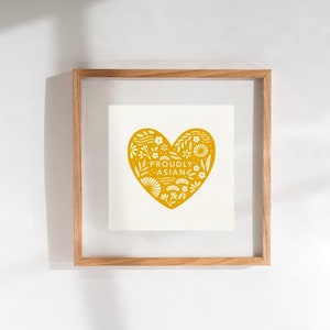 Può includere: Una stampa incorniciata con un design a forma di cuore giallo con dettagli floreali bianchi e il testo "Proudly Asian".