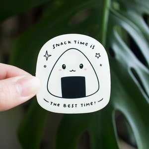 May include: White sticker with a cartoon onigiri, a Japanese rice ball, with a smiling face. The text reads "Snack time is the best time!"