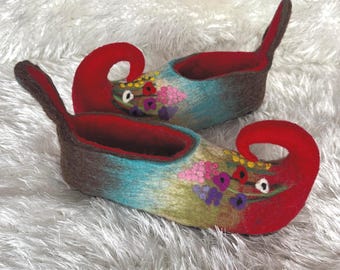 May include: A pair of whimsical felt slippers. The slippers feature a brown base with a turquoise and yellow gradient, red accents, and a curled toe. Floral embroidery in pink, purple, and yellow adorns the front.