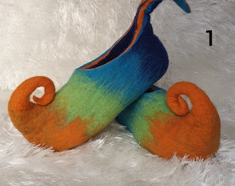 May include: A pair of colorful felt slippers with curled orange toes. The slippers are green, blue, and orange with a gradient effect. The slippers are on a white fluffy surface.