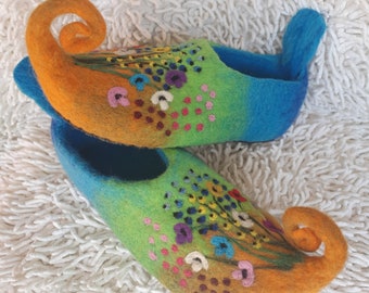 May include: A pair of colorful felt slippers with a whimsical design. The slippers are orange, green, and blue with embroidered flowers and a pointed toe.