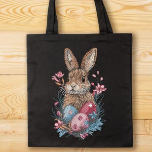 May include: A black tote bag with a brown rabbit embroidered on it. The rabbit is surrounded by pink flowers and blue and pink Easter eggs.