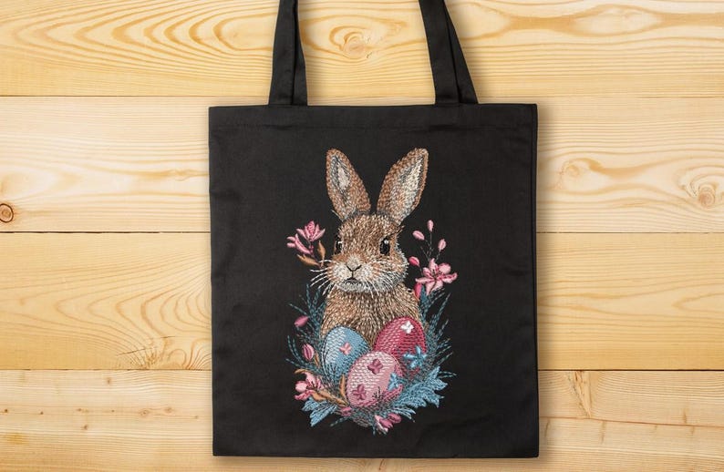 May include: A black tote bag with a brown rabbit embroidered on it. The rabbit is surrounded by pink flowers and blue and pink Easter eggs.