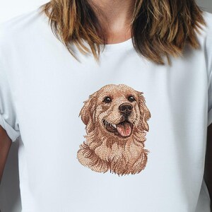 May include: White t-shirt with an embroidered Golden Retriever dog design. The dog's head is the focal point, with its tongue visible. The dog's fur is light brown. The shirt has short sleeves and is made of a soft material.