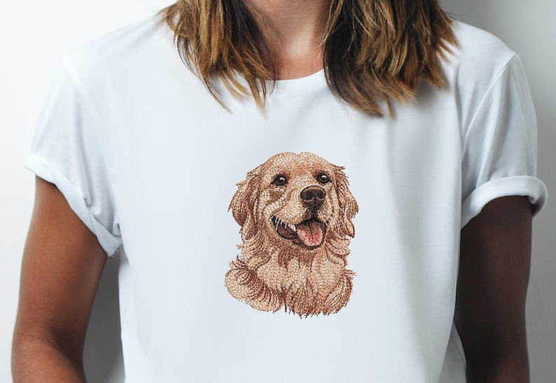 May include: White t-shirt with an embroidered Golden Retriever dog design. The dog's head is the focal point, with its tongue visible. The dog's fur is light brown. The shirt has short sleeves and is made of a soft material.