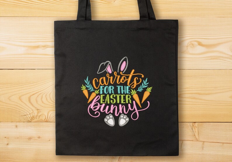 K&ouml;nnte beinhalten: Schwarze Einkaufstasche mit einem gestickten Design aus Karotten, Hasenohren und dem Text "Karotten f&uuml;r den Osterhasen".