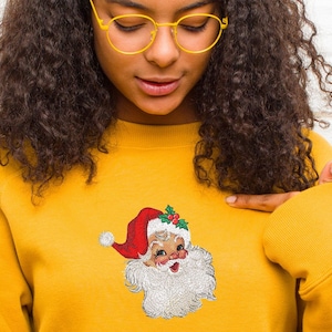 May include: A yellow sweatshirt with an embroidered image of Santa Claus on the front. The Santa Claus image is in a vintage style with a red hat, white beard, and a jolly expression.