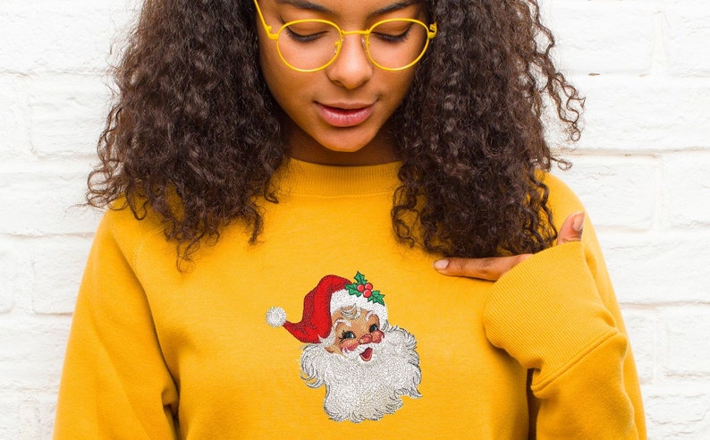 May include: A yellow sweatshirt with an embroidered image of Santa Claus on the front. The Santa Claus image is in a vintage style with a red hat, white beard, and a jolly expression.