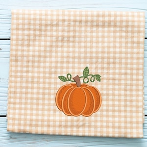 K&ouml;nnte beinhalten: Ein gestickter K&uuml;rbis in Braun und Orange mit einem gr&uuml;nen Stiel und Bl&auml;ttern auf einem beige-wei&szlig;en Gingham-Stoff.