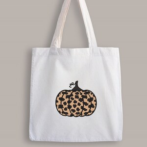 May include: A white tote bag with a black and brown leopard print pumpkin design.