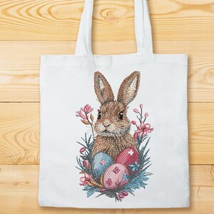 May include: A white tote bag with a brown bunny rabbit surrounded by pink flowers and blue and pink Easter eggs.