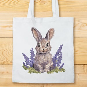 May include: A white tote bag with a brown rabbit embroidered on it. The rabbit is surrounded by purple flowers.