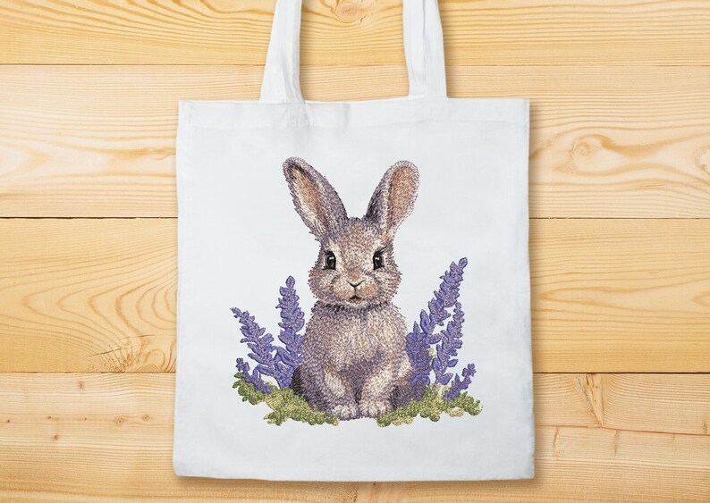 May include: A white tote bag with a brown rabbit embroidered on it. The rabbit is surrounded by purple flowers.