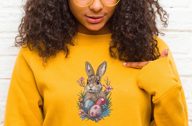 May include: A yellow sweatshirt with an embroidered design of a brown bunny rabbit holding Easter eggs surrounded by flowers.