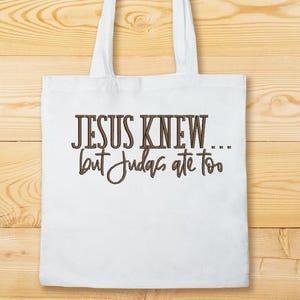 Puede incluir: Bolsa de tela blanca con texto marr&oacute;n que dice "JESUS KNEW... but Judas ate too".